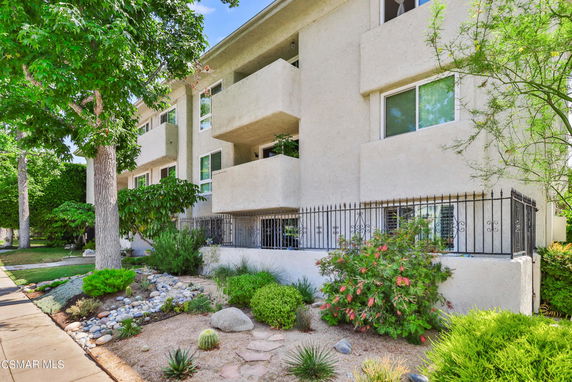 Front view of a multi-story residential building with balconies and a landscaped front area.
