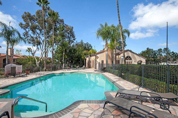 Outdoor swimming pool next to a residential building with lounge chairs and palm trees.