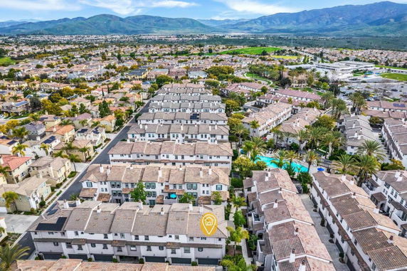 Aerial view of a residential area with multiple houses and a swimming pool, surrounded by mountains in the background.