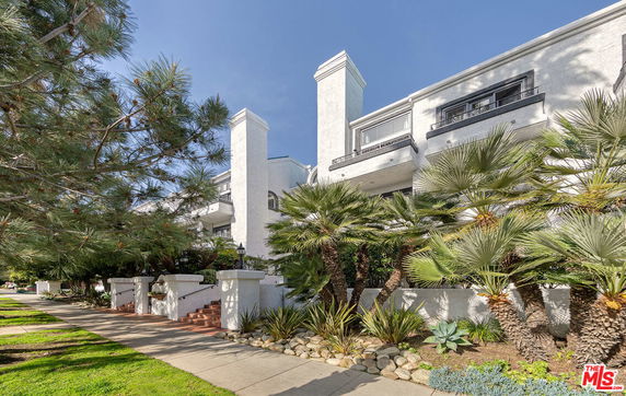 Front view of a multi-story white building with balconies and landscaped entrance.