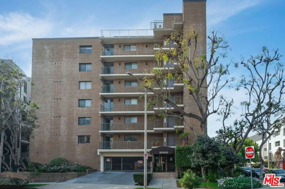 Front view of a multi-story apartment building with balconies and a brick facade.