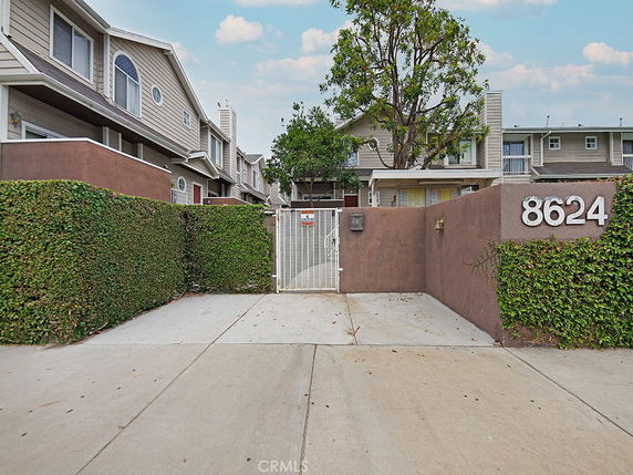 Front view of a multi-story house with a gated entrance and surrounding greenery.
