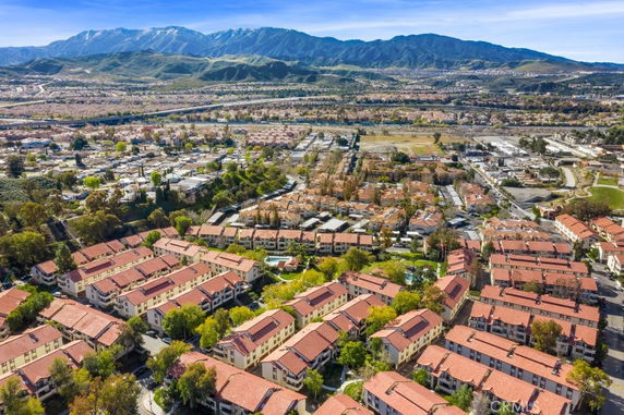 Aerial view of a sprawling residential area with rows of buildings having red roofs, surrounded by greenery and mountains in the background.