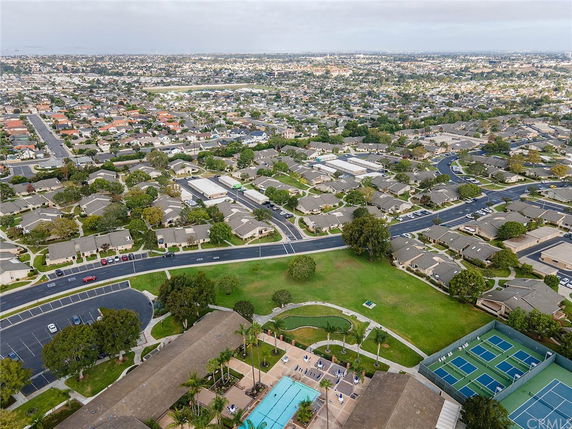 Wide aerial view of a residential area with numerous houses, roads, a swimming pool, and tennis courts.