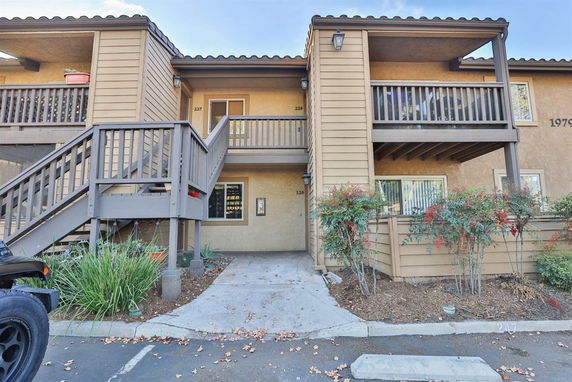 Front view of a two-story apartment building with wooden balconies and exterior staircases.