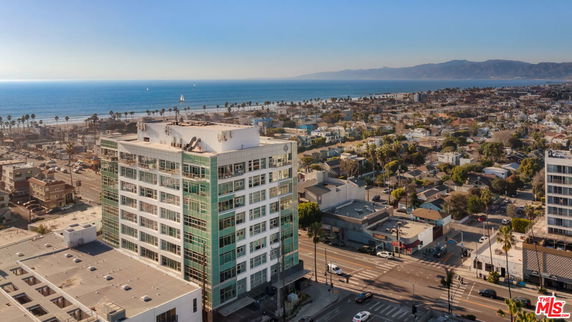 View of a multi-story building near a coastal area with sea and cityscape in the background.