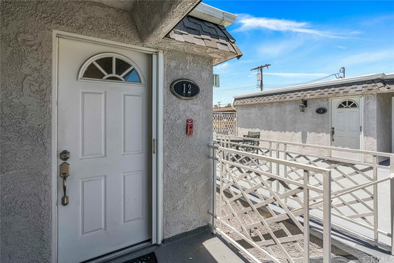 Entrance view of a residential unit with a white door, labeled number 12, small seating area, and adjacent similar units.