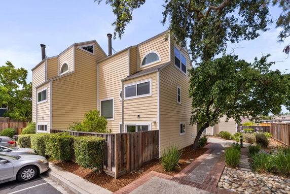 Front view of a multi-story beige house with distinct architectural features including multiple windows and chimneys.