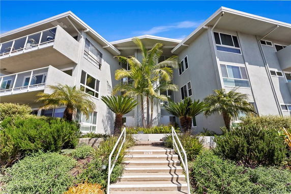 Front view of a modern multi-story building with balconies and a staircase leading to the entrance.