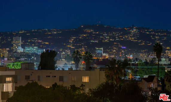 Panoramic view of a cityscape at night with illuminated buildings and hills in the background.