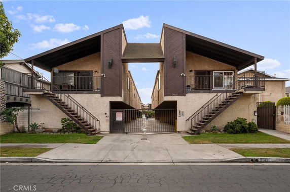 Front view of a multi-story residential building with external staircases and gated entry.