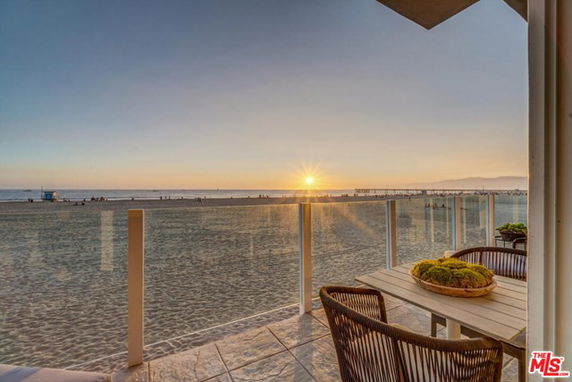 Panoramic view of a beach from a balcony with a seating area at sunset.