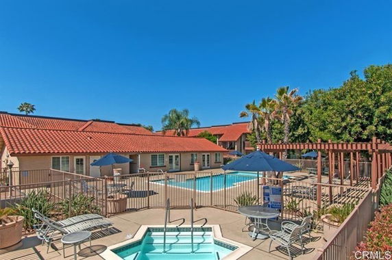 Outdoor swimming pool area with lounge chairs, umbrellas, and a hot tub in front of a building with a red roof.