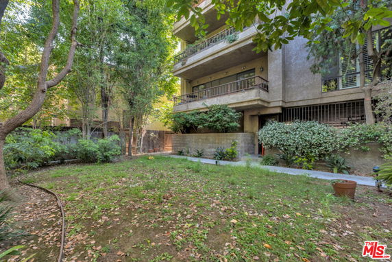 Front view of a multi-story building with balconies and surrounding garden.