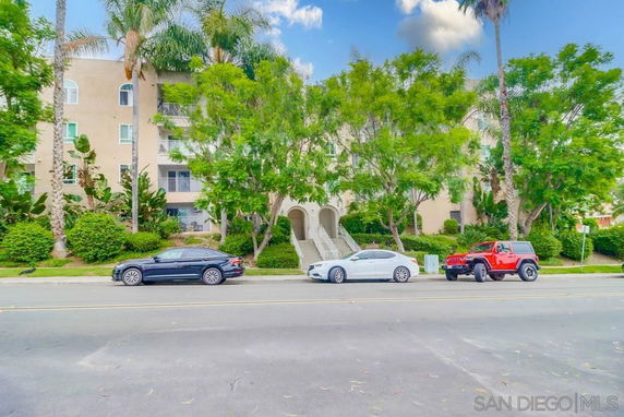 Front view of a multi-story apartment building with trees and parked cars.