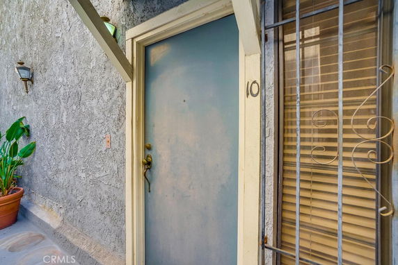 Front view of a door entrance with a stucco wall and window with bars.