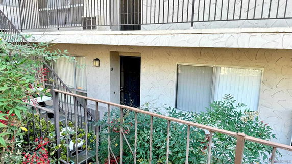 Front view of a multi-story building entrance with railings and plants.