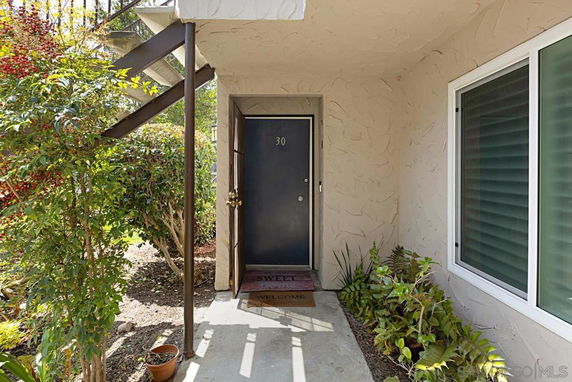 Front entrance of a residential unit with a black door and number 30. There is a welcome mat and some plants near the entrance.