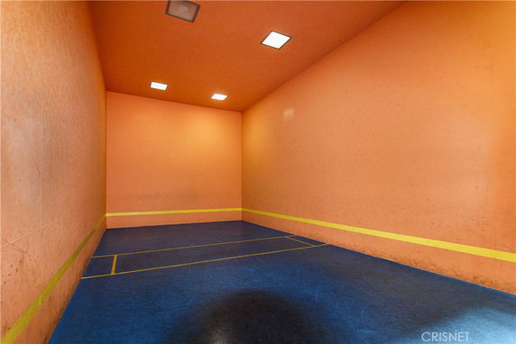 Interior view of an indoor squash or racquetball court with orange walls and blue floor.