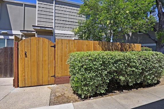 Front view of a house with a wooden gate and hedge at the entrance.