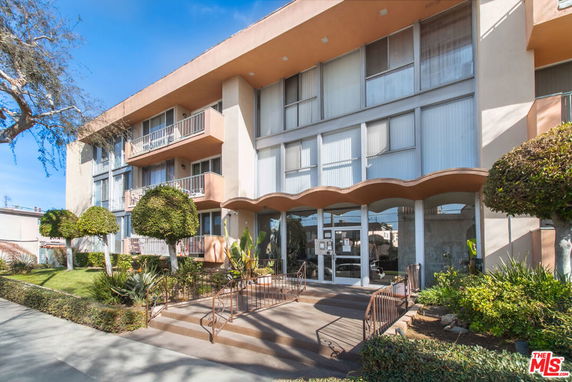 Front view of a multi-story residential building with balconies and a landscaped entrance.
