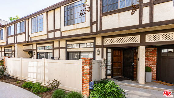 Front view of a two-story house with a white fence and wooden accents.