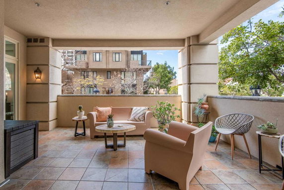Covered outdoor patio with seating and view of nearby building and trees.