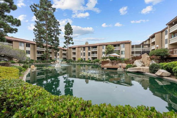 View of a multi-story residential building complex surrounded by a pond and trees.