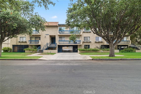 Front view of a multi-story apartment building with balconies and a tiled roof.