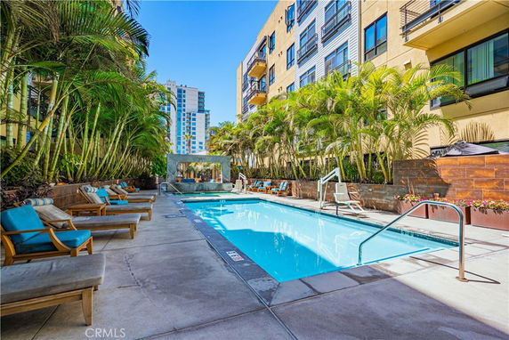 Outdoor swimming pool adjacent to a multi-story building with lounging chairs and potted plants.