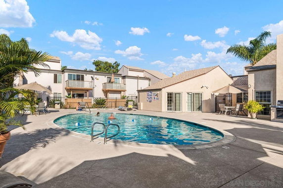 Outdoor swimming pool area with adjacent buildings and lounge chairs.