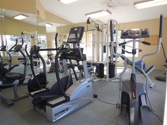 Indoor gym area with exercise machines and mirrors on the walls.