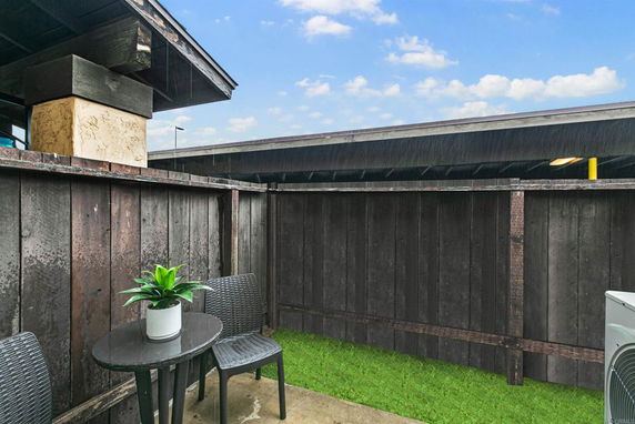 Outdoor area with a small table, two chairs, and a potted plant next to a wooden fence.