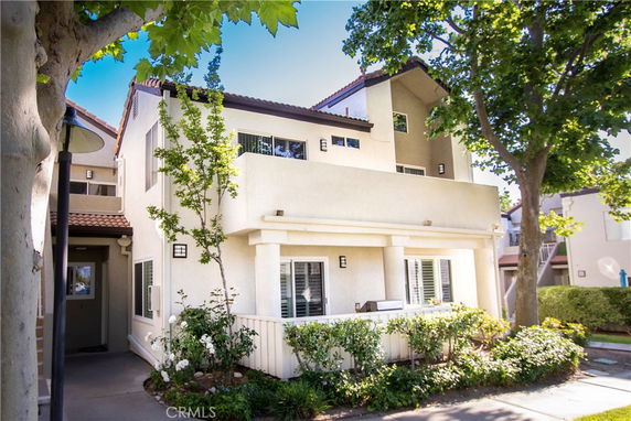 Front view of a two-story house with a large balcony and surrounding greenery.