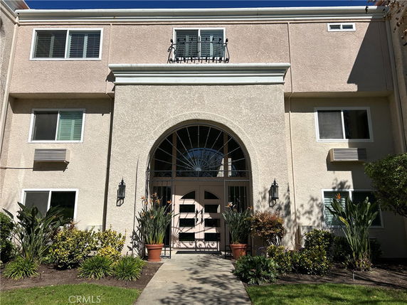 Front view of a beige-colored apartment building with large arched entrance and multiple windows.