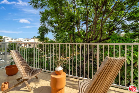 Panoramic view from a balcony with chairs and potted plants overlooking trees and buildings.