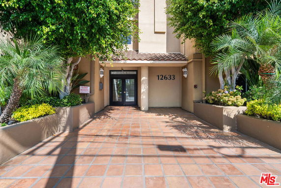 Front view of a building entrance with tiled flooring and surrounding greenery.