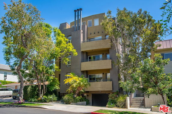 Front view of a multi-story residential building with balconies and trees nearby.
