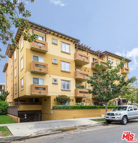 Front view of a multi-story apartment building with balconies and a parking area.
