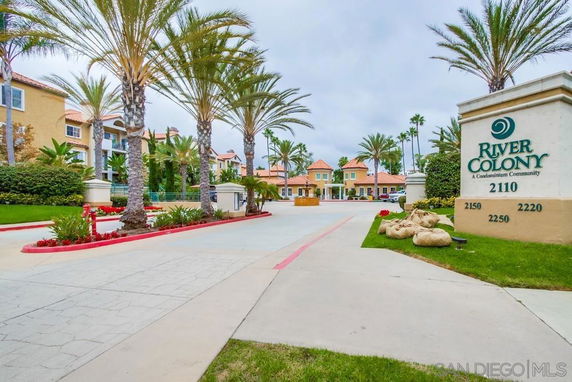 Front view of a condominium community entrance with palm trees and sign.
