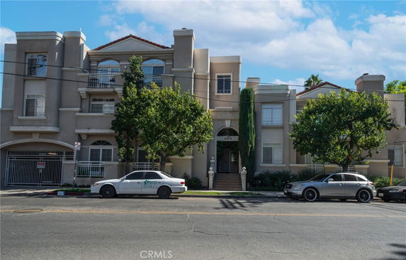 Front view of a multi-story apartment building with decorative balconies and multiple parked cars in front.
