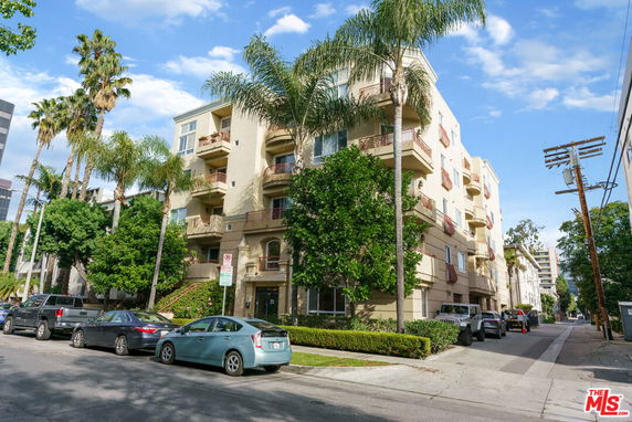 Front view of a multi-story building with balconies and palm trees nearby.