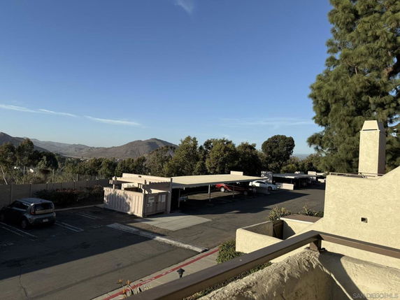 Outdoor parking with covered parking spots and cars, surrounded by trees and hills.