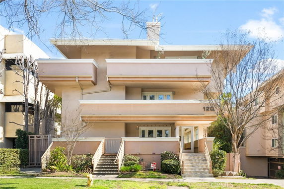 Front view of a multi-story residential building with balconies and staircase entrance.