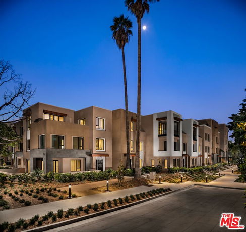 Front view of a modern multi-story apartment building with large windows and a landscaped walkway.