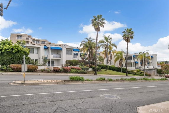 Front view of a modern multi-story building complex with blue awnings and palm trees.