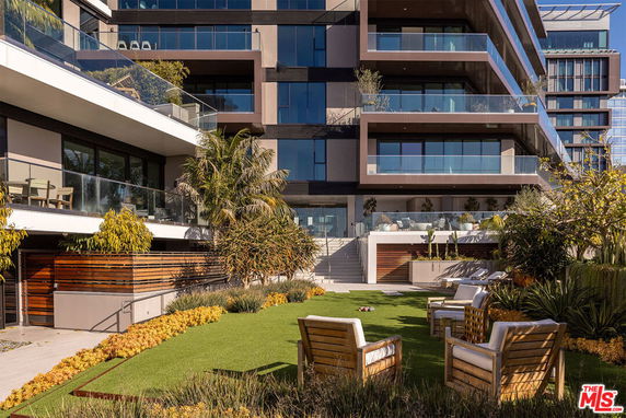 Front view of a modern multi-story apartment building with balconies and landscaped garden area.