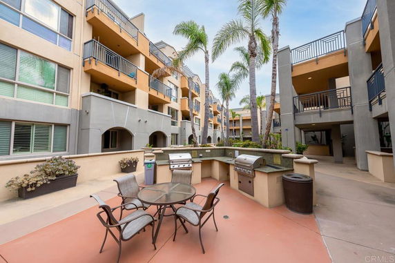 Outdoor patio area with barbecue grills and seating in a multi-story apartment complex.