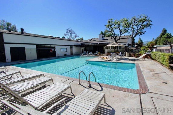 Outdoor swimming pool area with lounge chairs and an umbrella near a building.