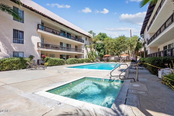 Outdoor area with a swimming pool and adjacent hot tub, surrounded by multi-story residential buildings.